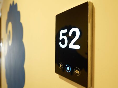 A sign with number 52. The sign is a black panel mounted in a yellow wall. The panel have a blue color bell sign litted.の写真素材