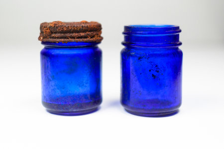 Aged and patina vintage blue glass medical bottles on a white and gray background with copy space and a rusted cap.の写真素材