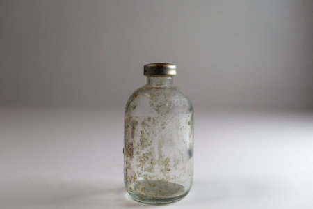 One dirty clear glass medical vaccine bottle, aged and patina on a white background.  Empty and covered with dirt and rust.の写真素材