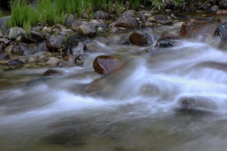 A river flowing over rocks with green grass in the backgroundの写真素材