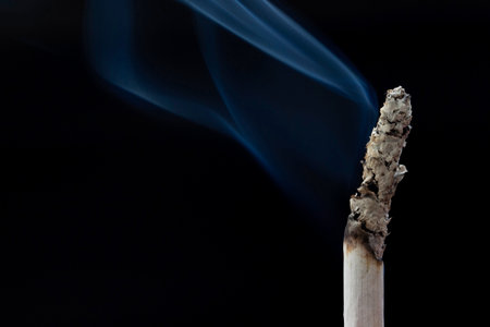close up of burning cigarette with black background and cigarette smokeの写真素材