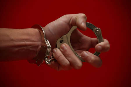 A really expressive photograph of a hand (handcuffed) holding the other end of the cuffs, on a red background! :)の写真素材