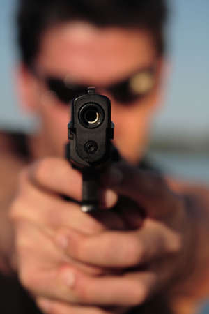 A man holding a pistol and pointing it at the camera. (This image is part of a series).