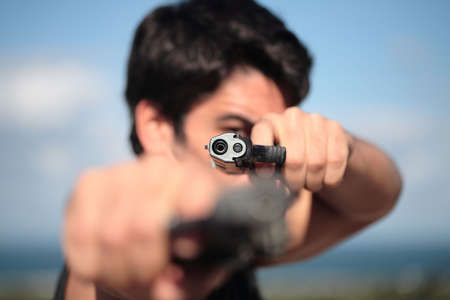 A young man pointing 2 pistols at the camera.の写真素材