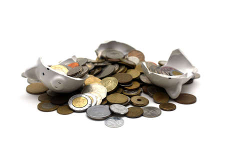 A broken piggy bank isolated on a white background with loads of coins from around the world.の写真素材