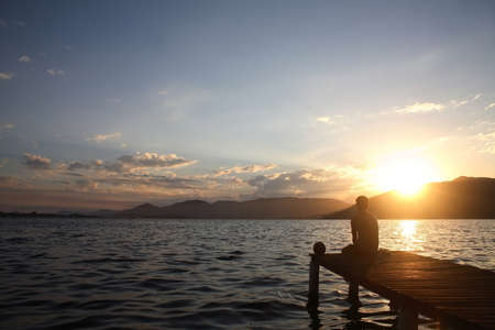 A young man, sitting on a pier, watching the sunset!の写真素材