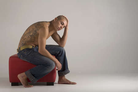 A young, muscular brazilian man in a studio shot, on a red seat, on a gray background.の写真素材