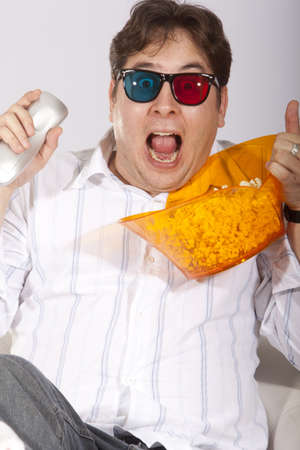A young man watching a movie in 3D, with stylish 3D glasses and eating popcorn.の写真素材