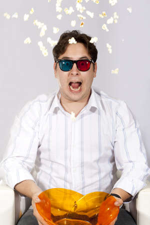 A young man watching a movie in 3D, with stylish 3D glasses and eating popcorn. He got so scared he threw his popcorn into the air.の写真素材