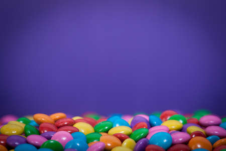 A bunch of chocolate buttons, in various colors such as pink, purple and yellow with a blue background.の写真素材