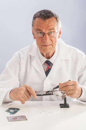 An older male wearing a white lab coat and repairing electronic equipments, like a technician or a repair man.の写真素材