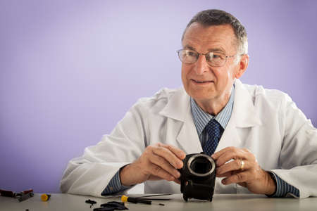 An older male wearing a white lab coat and repairing electronic equipments, like a technician or a repair man.の写真素材