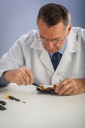An older male wearing a white lab coat and repairing electronic equipments, like a technician or a repair man.の写真素材