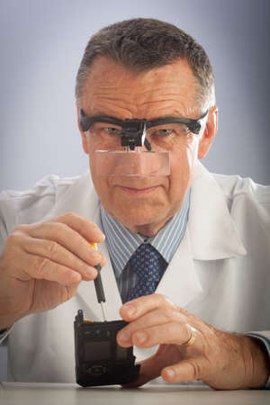 An older male wearing a white lab coat and repairing electronic equipments, like a technician or a repair man.の写真素材