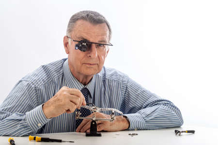 An older man wearing a shirt and tie, repairing a watch.の写真素材