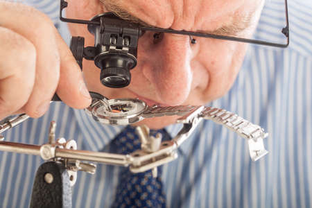 An older man wearing a shirt and tie, repairing a watch.の写真素材