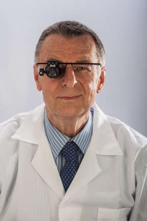 An older male wearing a white lab coat and repairing electronic equipments, like a technician or a repair man.の写真素材