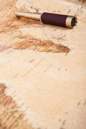 An antique, out of focus, map with a beautiful golden and leather telescope.の写真素材