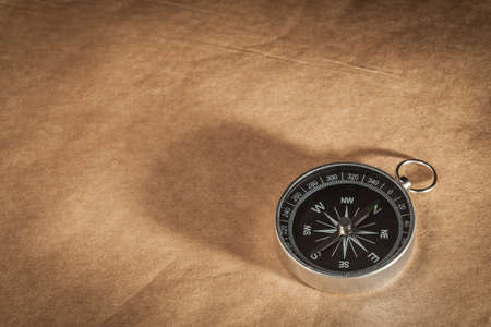 A silver compass with black face pointing north on a brown paper background.の写真素材