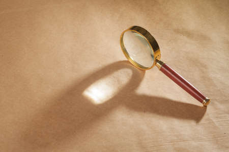 A golden and red magnifying glass on a brown paper background.の写真素材