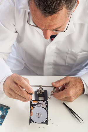 An older male wearing a white lab coat and repairing electronic equipments, like a technician or a repair man.の写真素材