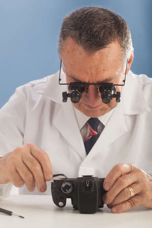 An older male wearing a white lab coat and repairing electronic equipments, like a technician or a repair man.の写真素材