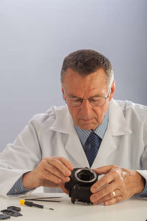 An older male wearing a white lab coat and repairing electronic equipments, like a technician or a repair man.の写真素材