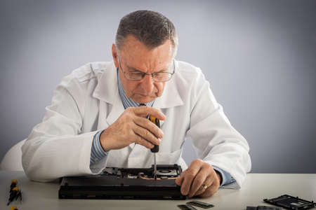 An older male wearing a white lab coat and repairing electronic equipments, like a technician or a repair man.の写真素材