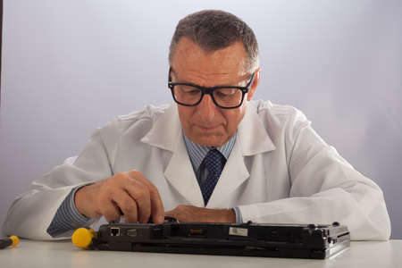An older male wearing a white lab coat and repairing electronic equipments, like a technician or a repair man.の写真素材