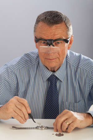An older man wearing a shirt and tie, repairing a watch.の写真素材