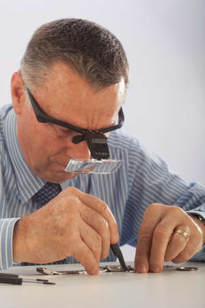 An older man wearing a shirt and tie, repairing a watch.の写真素材