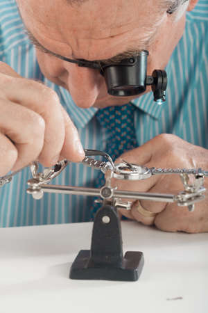 An older man wearing a shirt and tie, repairing a watch.の写真素材