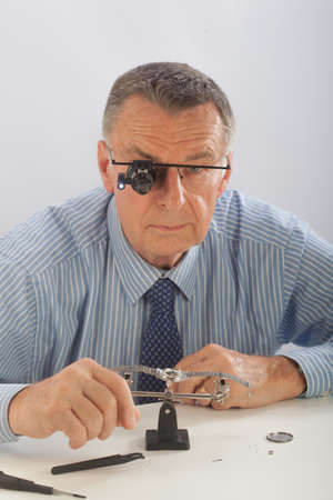An older man wearing a shirt and tie, repairing a watch.の写真素材
