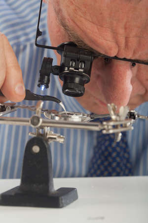 An older man wearing a shirt and tie, repairing a watch.の写真素材