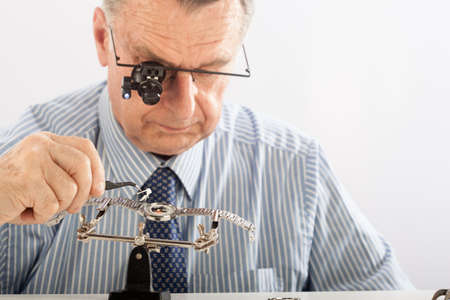 An older man wearing a shirt and tie, repairing a watch.の写真素材