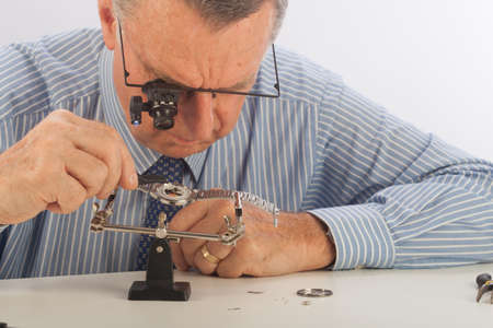 An older man wearing a shirt and tie, repairing a watch.の写真素材