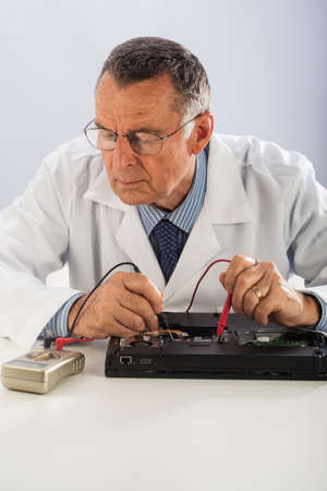 An older male wearing a white lab coat and repairing electronic equipments, like a technician or a repair man.の写真素材