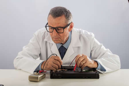 An older male wearing a white lab coat and repairing electronic equipments, like a technician or a repair man.の写真素材