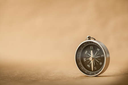 A silver compass with black face pointing north on a brown paper background.の写真素材