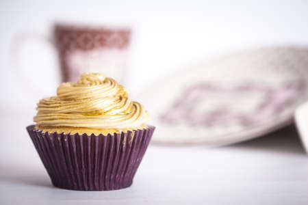 A cupcake in front of plates and a mug, on a white background.の写真素材