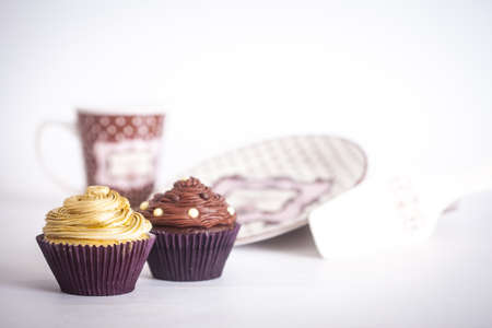 Cupcakes in front of plates and a mug, on a white background.の写真素材