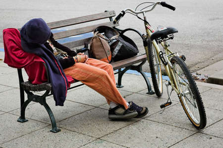 A homeless person trying to sleep on a bench.の写真素材