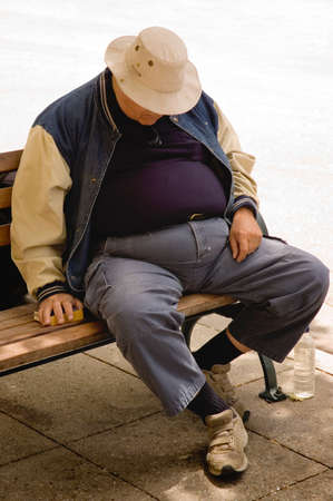 A heavy older gentleman who has fallen asleep on a city bench.の写真素材