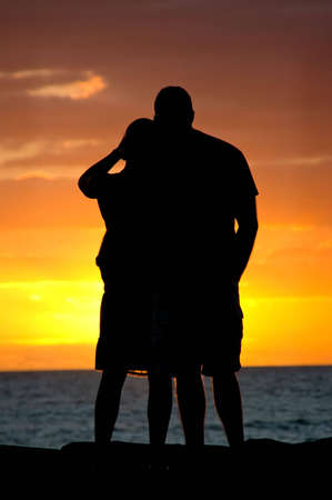 Silhouette of a young couple in a tropical location watching the sun set.の写真素材