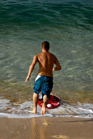 A teenaged boy at the beach running to jump onto a boogie boardの写真素材