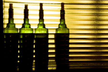 Four green bottles sitting behind a rippled glass window.の写真素材