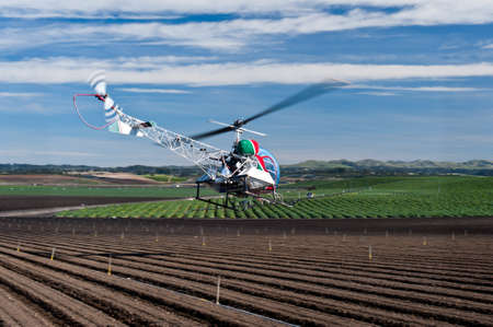Helicopter spraying pest control chemicals on crops raised conventionally.のeditorial素材