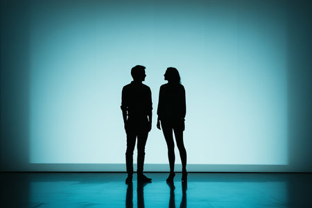 A silhouetted man and woman stand facing each other against a bright blue backdrop, creating a stark...