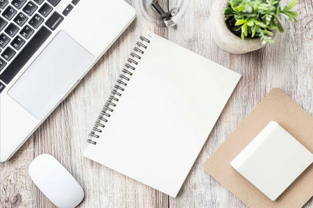 A clean and organized desk setup featuring a laptop computer, an open notebook, a computer mouse, and a small potted plant on a wooden surface.の写真素材