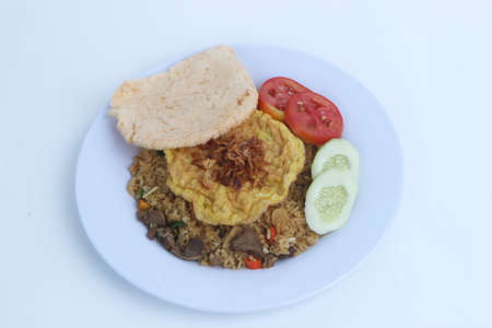 Nasi goreng fried rice with pete and egg garnished with fresh cucumber slices and prawn crackers on a plate on a cloth. Asian food.の写真素材